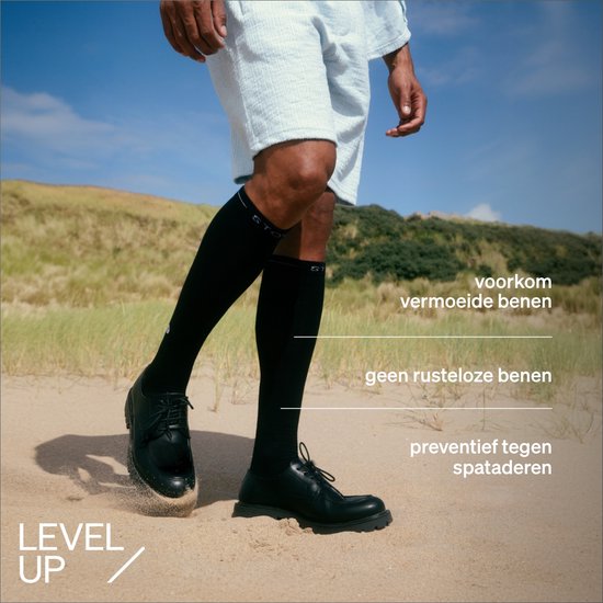 Man in zwarte STOX compressiekousen en blauwe shorts op een strand.