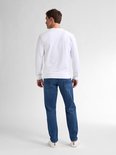 Achteraanzicht van een model in een wit shirt en blauwe tapered fit jeans.