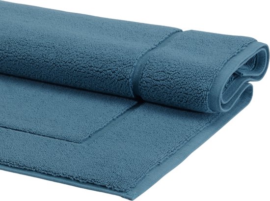 Blauwe badmat, opgerold, met zichtbare textuur en een opstaande rand.