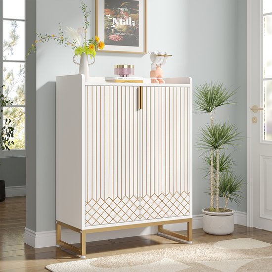 Witte schoenenkast met gouden lijnen en gouden handgrepen, gesloten, naast planten en een schilderij.