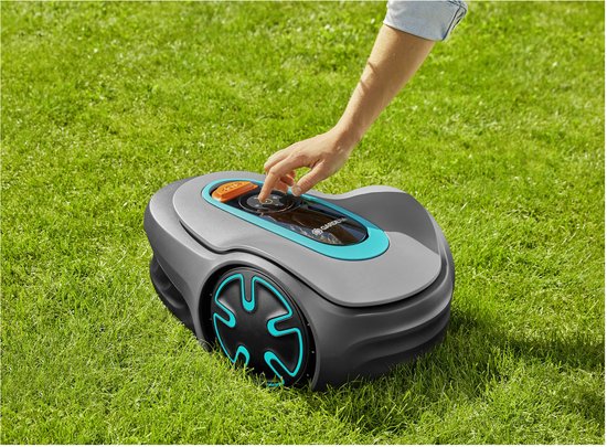 Hand bedient de robotmaaier op het gras met een oranje stopknop en turkooizen accenten.