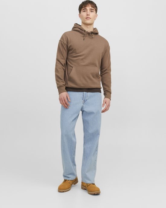 Man in een lichtblauwe jeans en een bruine hoodie, met bruine laarzen.