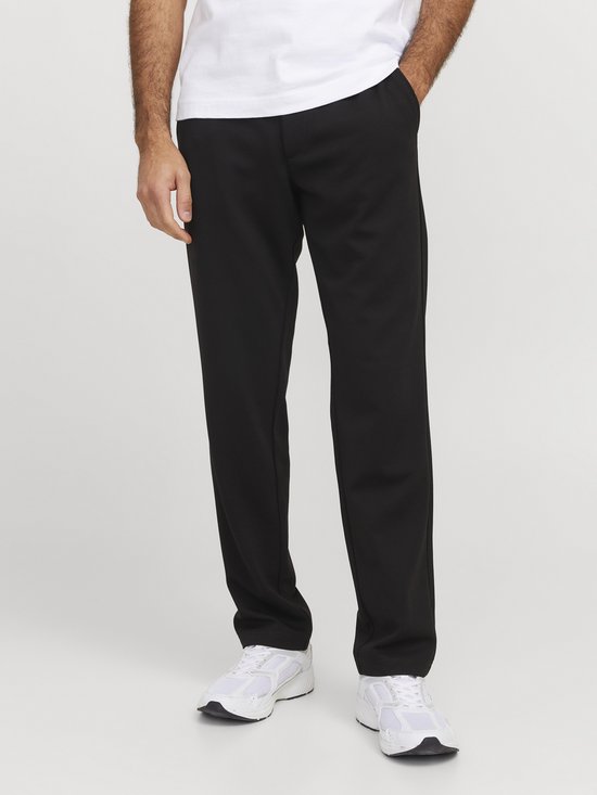 Man die een zwarte joggingbroek draagt met een wit t-shirt en witte sneakers.