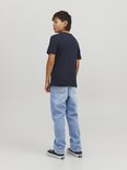 Jongen van achteren gezien, in een lichtblauwe, wijde spijkerbroek en donker T-shirt.