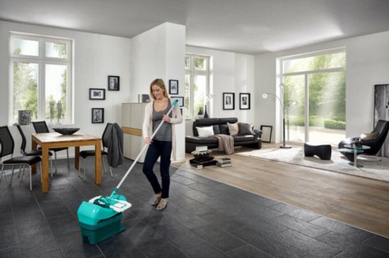Femme nettoyant le sol avec une serpillière et un seau turquoise dans un salon moderne.