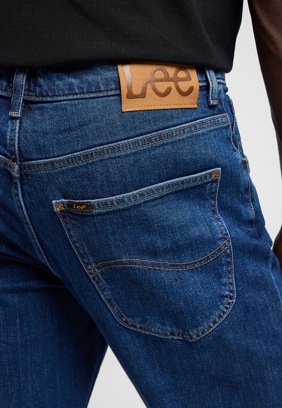 Close-up van de achterkant van een blauwe Lee jeans, met een bruin Lee logo op de tailleband.