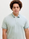 Close-up van een man met krullend haar, draagt een lichtgroen poloshirt met geborduurd logo.