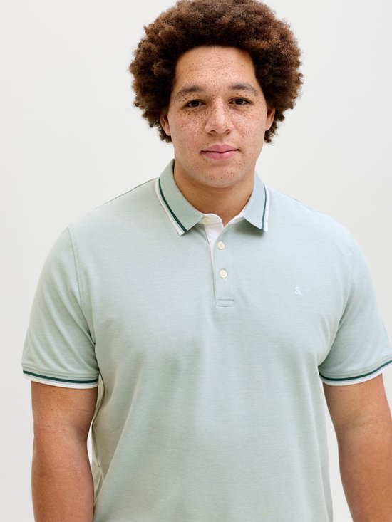 Close-up van een man met krullend haar, draagt een lichtgroen poloshirt met geborduurd logo.