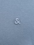 Close-up van de stof van een blauw poloshirt met een geborduurd logo.