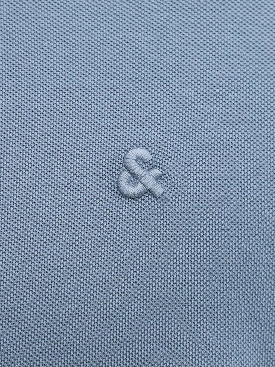 Close-up van de stof van een blauw poloshirt met een geborduurd logo.