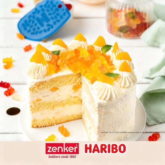 Gâteau avec glaçage blanc et décoration HARIBO, à côté d'une corne de boulanger bleue avec motif d'ours.
