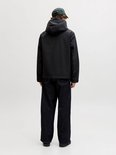 Man draagt zwarte jas met capuchon en jeans. Van de achterkant.