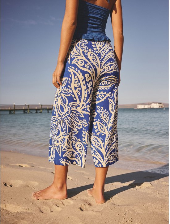 Vrouw draagt een culotte met blauwe en crème paisley print op het strand.