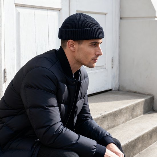 Man met een donkerblauwe beanie en een donkerblauwe jas, zittend op trappen.