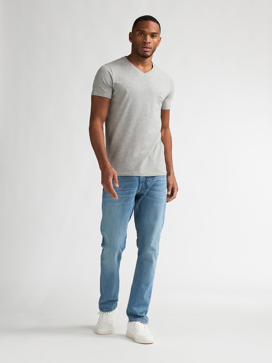 Man draagt een effen lichtgrijs T-shirt met V-hals en een lichtblauwe jeans.