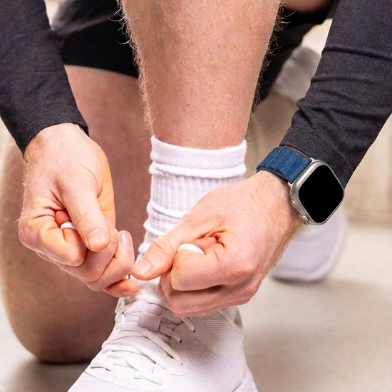 Man strikt witte schoenen. Donkerblauw nylon bandje om zijn pols, bevestigd aan een zilverkleurige Apple Watch.