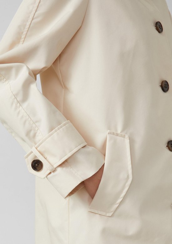 Crèmekleurige trenchcoat, detail van de mouw met klep en knoop, en een zak.