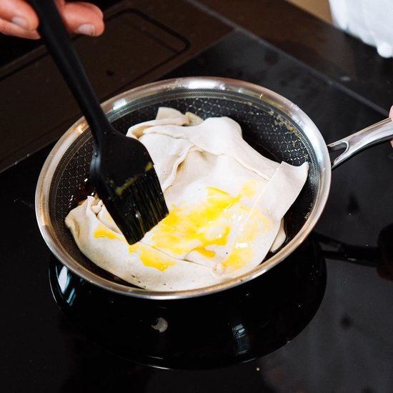 Chef bestrijkt deeg in een zilverkleurige koekenpan met eigeel.