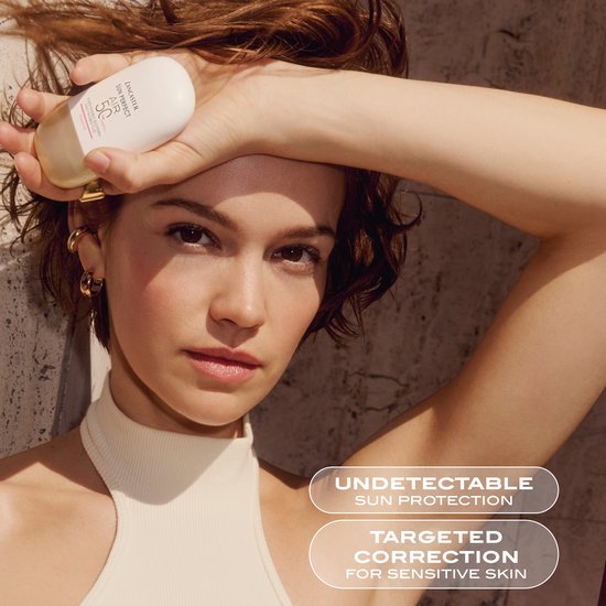Model met een witte top, houdt een witte en gouden zonnebrandcrème fles vast.