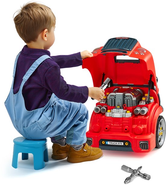 Jongen met blauwe overall zit op blauwe kruk en repareert rode speelgoedtruck met motor en gereedschap.