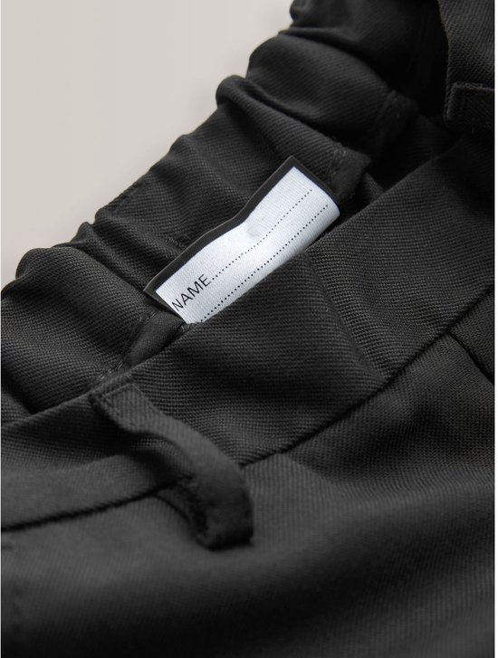 Label 'NAME' op de tailleband van een zwarte broek.