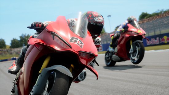 Close-up van een rode race motor met nummer 63 op de voorkant, coureur met helm, andere motor op achtergrond.