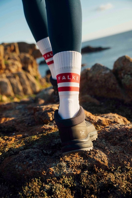 Voeten in witte sokken met rode strepen en 'FALKE' opdruk, wandelend op rotsen bij de zee.