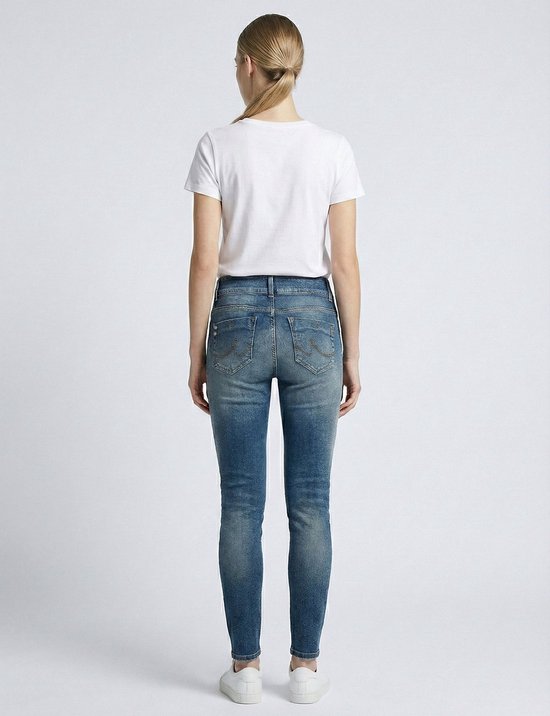 Model van achteren in een witte t-shirt en een nauwsluitende, lichtblauwe spijkerbroek met distressed details.