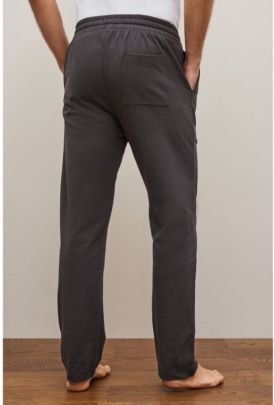 Man met handen in zakken van een donkergrijze joggingbroek met achterzak.