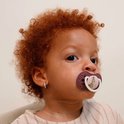 Een baby met krullend rood haar met een roze speen met een konijn erop.