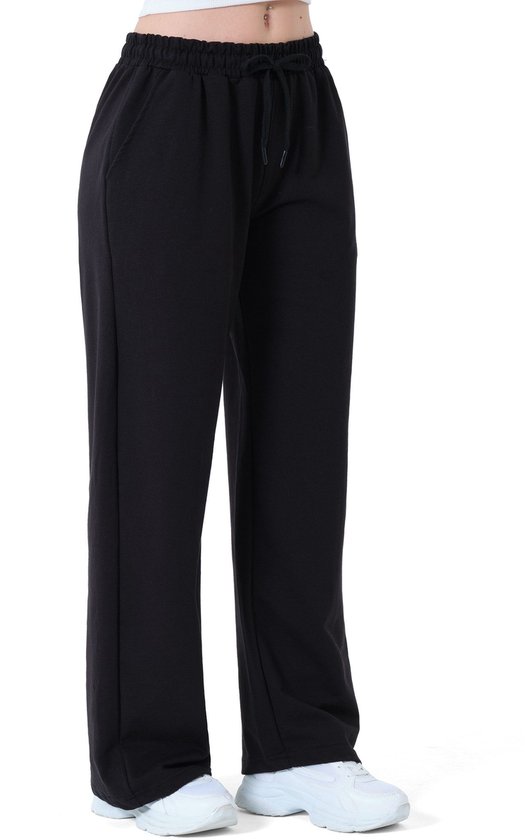 Zij-aanzicht van een zwarte wijde joggingbroek met trekkoord en witte sneakers.