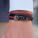 Dichtbij van een leren armband met zwart en rood vlechtwerk en een zwarte gesp met leeuwenlogo.