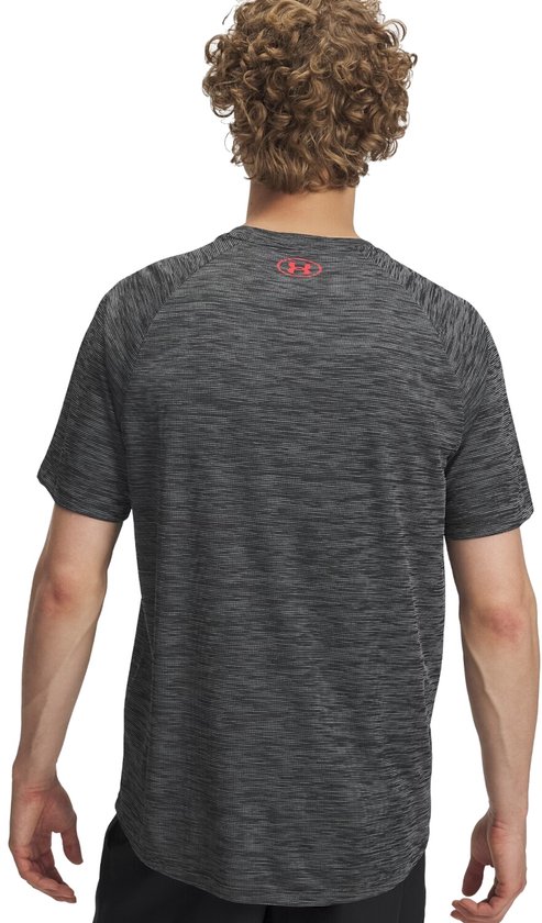 Man draagt een zwart gestreept sportshirt met rood Under Armour logo op de achterkant.