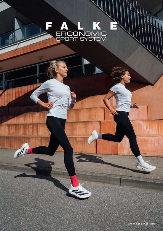 Twee vrouwen rennen op een stoep langs een gebouw. De ene vrouw draagt een lange witte mouwshirt, zwarte legging en witte schoenen met rode sokken. De andere draagt een witte t-shirt, zwarte legging en witte schoenen.