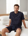 Man in blauw pyjamashort met ruitpatroon, zittend op een bed.