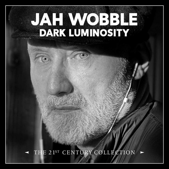 Portret van Jah Wobble met een pet, "Dark Luminosity" en "The 21st Century Collection" op de hoes.