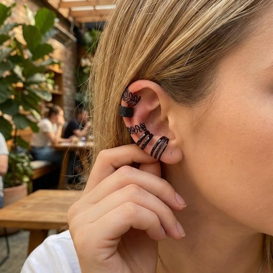 Vrouw met goudblond haar draagt vijf zwarte oorclips: reliëf, blad, spiraal en drievoudige ringen.