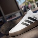 Witte sneaker met zwarte Adidas strepen en bruine zool, gefotografeerd op straat.