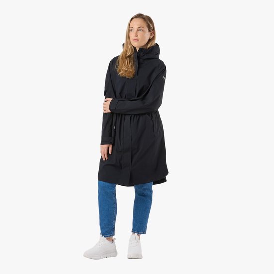 Femme debout dans un long manteau noir à capuche, un jean et des baskets blanches.