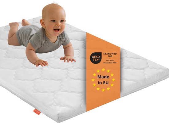 Een baby kruipt op een witte, gewatteerde matras met een Oeko-Tex label 'Made in EU'.