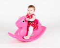 Een baby met een rood-wit gestippelde jurk, zittend op een roze Little Tikes hobbelpaard.