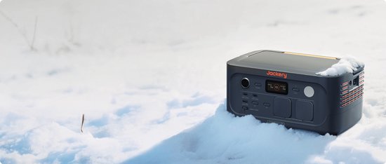 Donkergrijs Jackery Explorer 500 powerstation met oranje accenten, in de sneeuw.