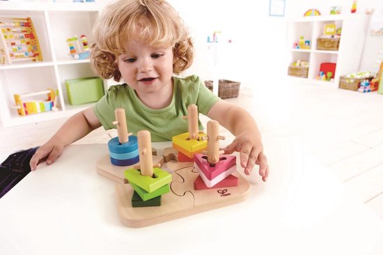 Een jong kind met krullend blond haar speelt met de Hape Steckpuzzle met blauwe, groene, gele en roze vormpjes.