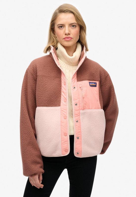 Model draagt bruine, roze en lichtroze fleece jas met hoge kraag.