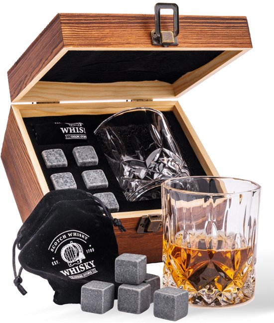 Une boîte en bois ouverte avec un verre, un sac noir et des pierres grises. Un verre de liquide ambré se trouve à côté.