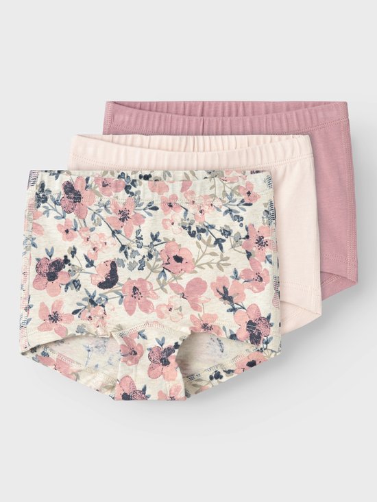 Drie meisjesbroekjes, waarvan één met een roze en blauwe bloemenprint, op een grijze achtergrond.