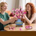 Deux femmes souriantes à table avec un bouquet de fleurs de cerisier roses dans un vase bleu.