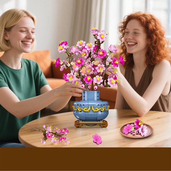 Deux femmes souriantes à table avec un bouquet de fleurs de cerisier roses dans un vase bleu.