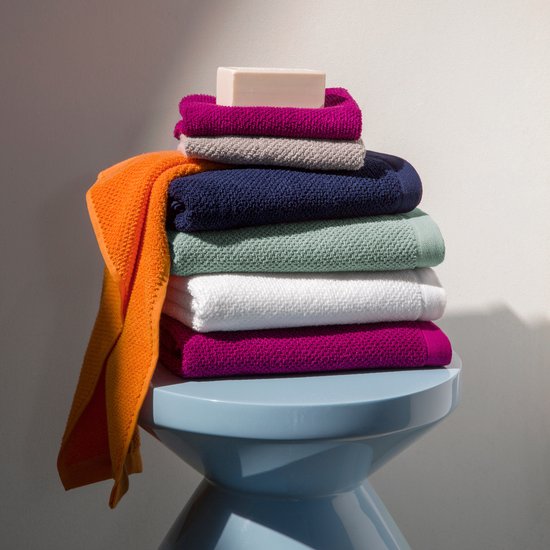 Stapel handdoeken met een zeepje erop. Kleuren zijn oranje, paars, grijs, marineblauw, mintgroen en wit.
