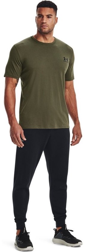 Man in groen Under Armour sportshirt met zwart logo, gedragen met zwarte trainingsbroek.